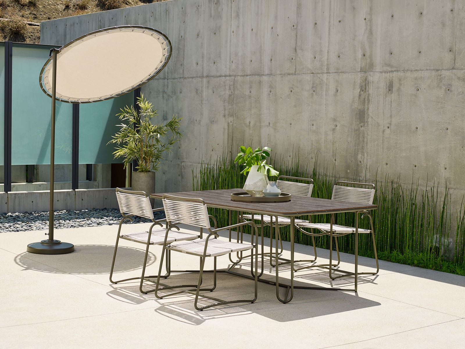 Walter Lamb aluminum dining table from Brown Jordan outdoor furniture on patio in front of a tall wall with a green floral centerpiece