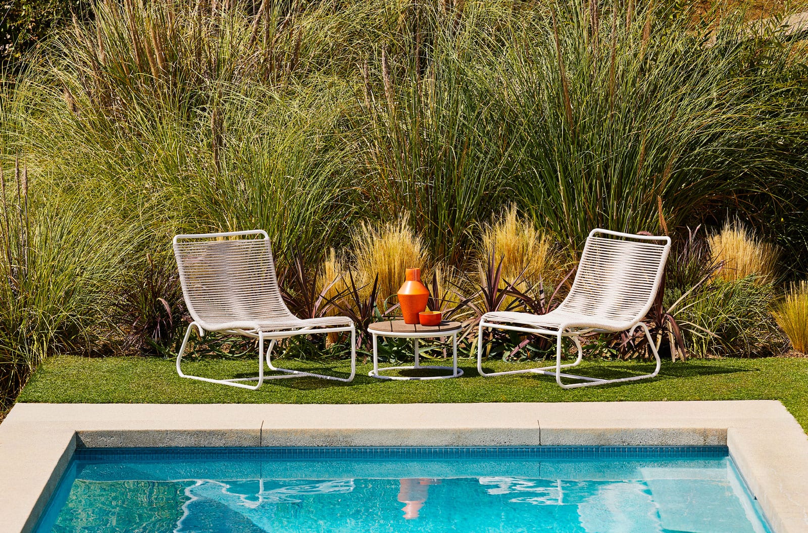 Walter Lamb aluminum lounge chairs from Brown Jordan outdoor furniture placed on grass facing a swimming pool with a decorative landscape background