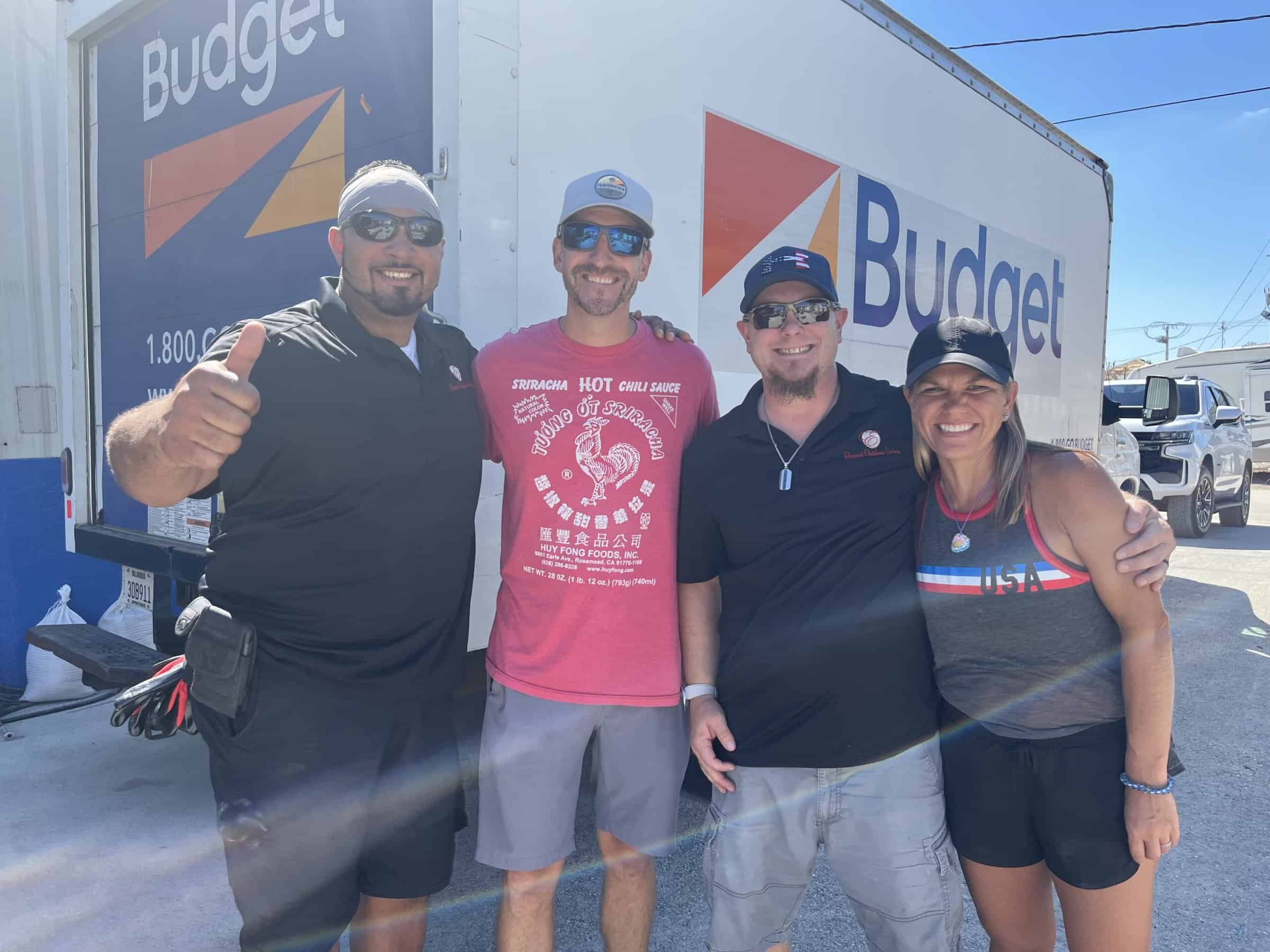 Elegant Outdoor Living's crew smiling posing together from left to right Al (left), owner Nate (middle left), CJ (middle right), and Stephanie (right) in front of a box truck full of donations at the FMB Strong charity location